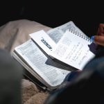 person holding black pen and writing on white notebook